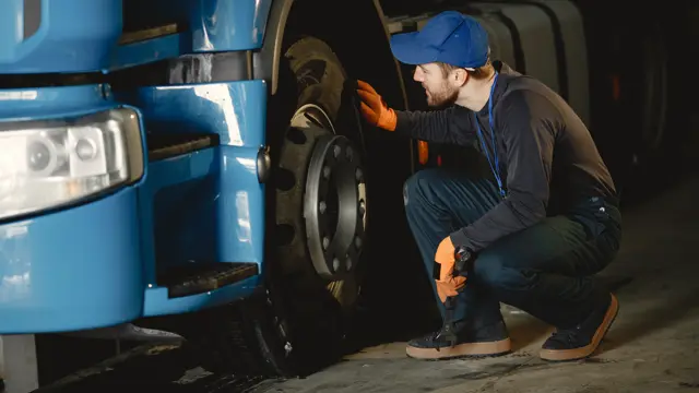 Mechanic checking the front wheel of a blue truck in a workshop