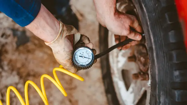Hands checking tyre pressure with a gauge and air line