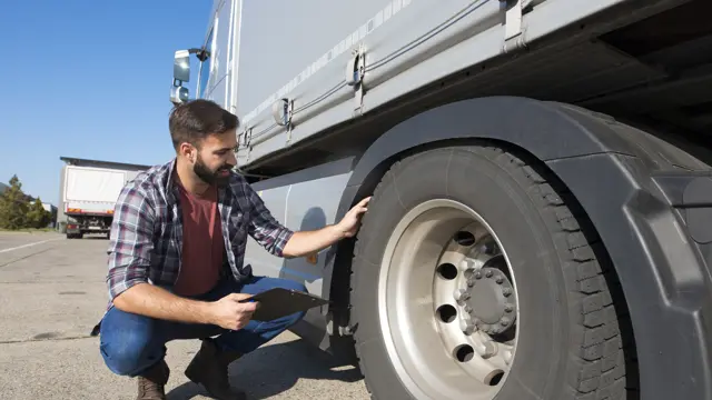 Truck driver kneeling to check the tread depth of a truck tyre